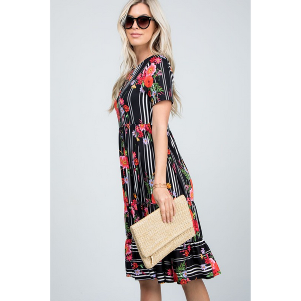 side view of woman wearing black floral midi dress and holding a purse.