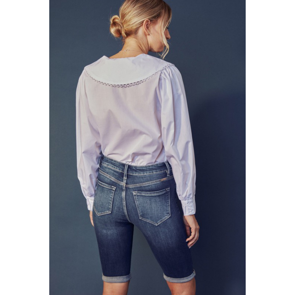 rear view of woman wearing light blue collared blouse and denim Bermuda shorts.